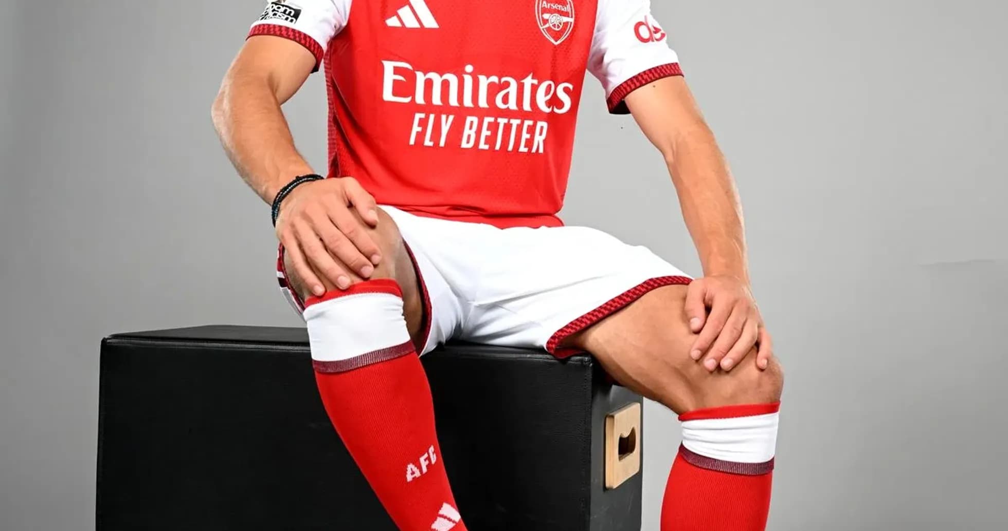 Jugador sentado con balón, vistiendo camiseta del Arsenal