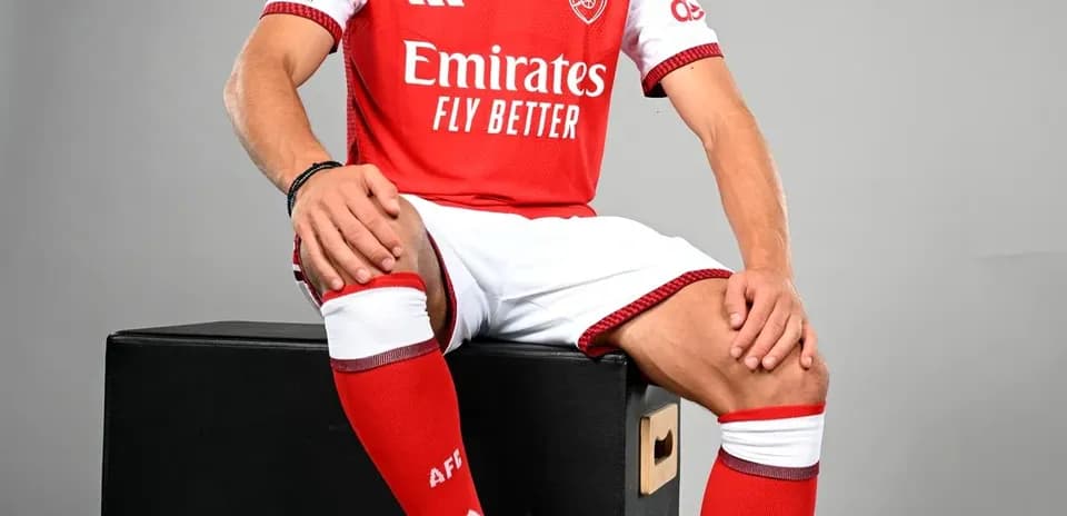 Jugador sentado con balón, vistiendo camiseta del Arsenal
