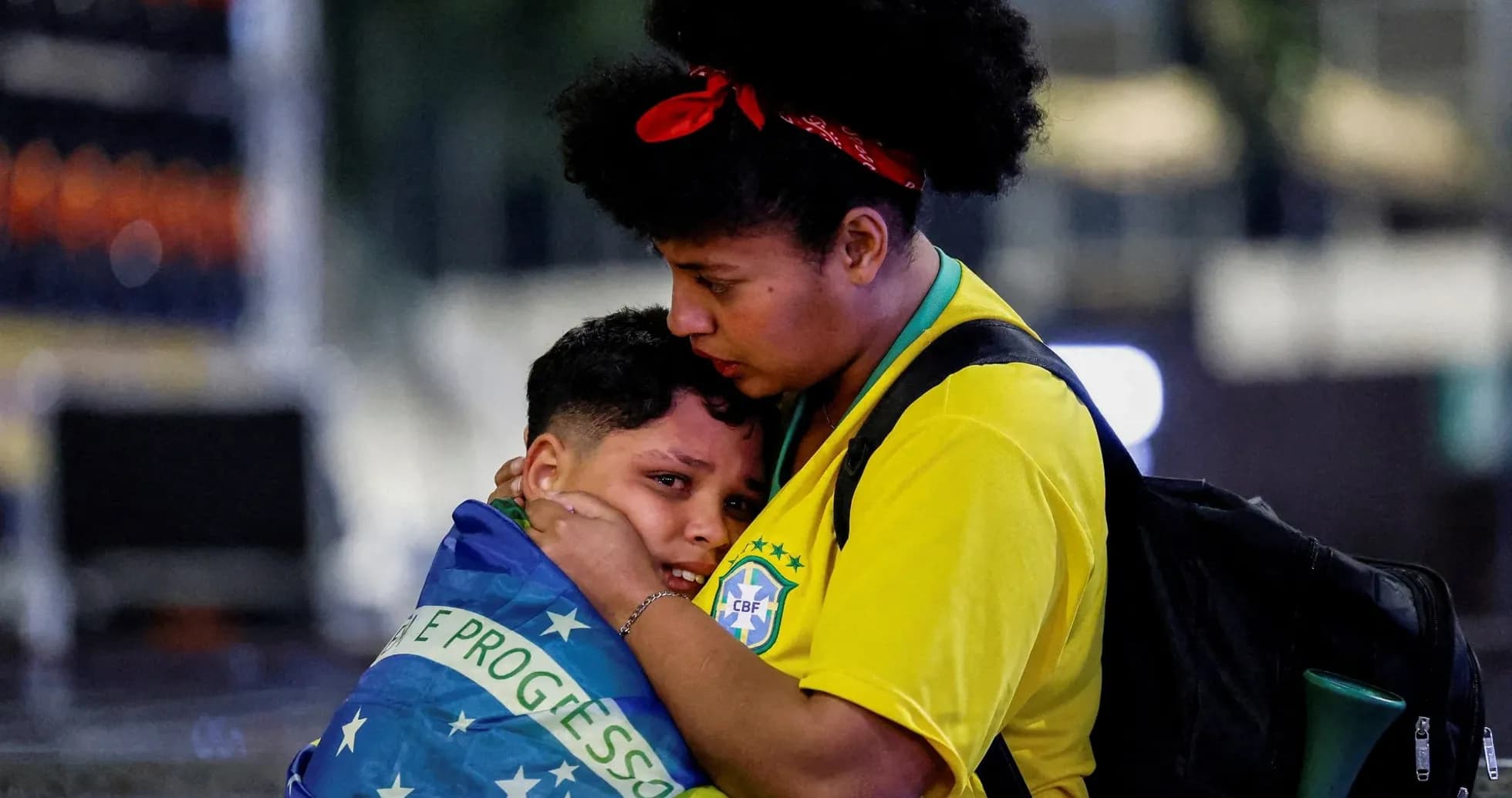 Mujer abrazando a niño envuelto en bandera de Brasil