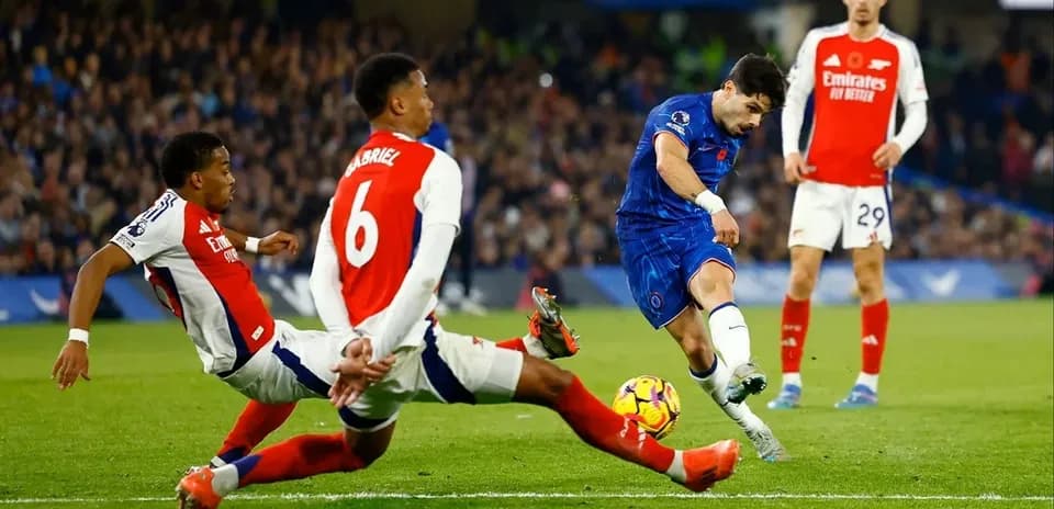 Jugador de Chelsea disparando mientras dos defensores de Arsenal intentan bloquear