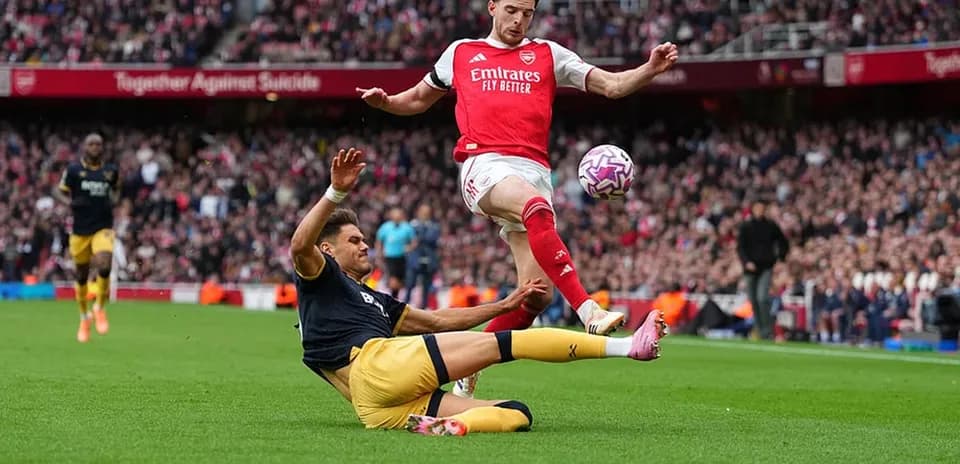 Jugador de Arsenal saltando sobre oponente caído