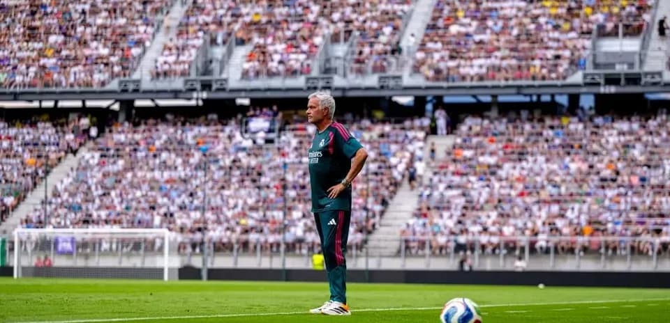 Entrenador de pie en campo con público detrás