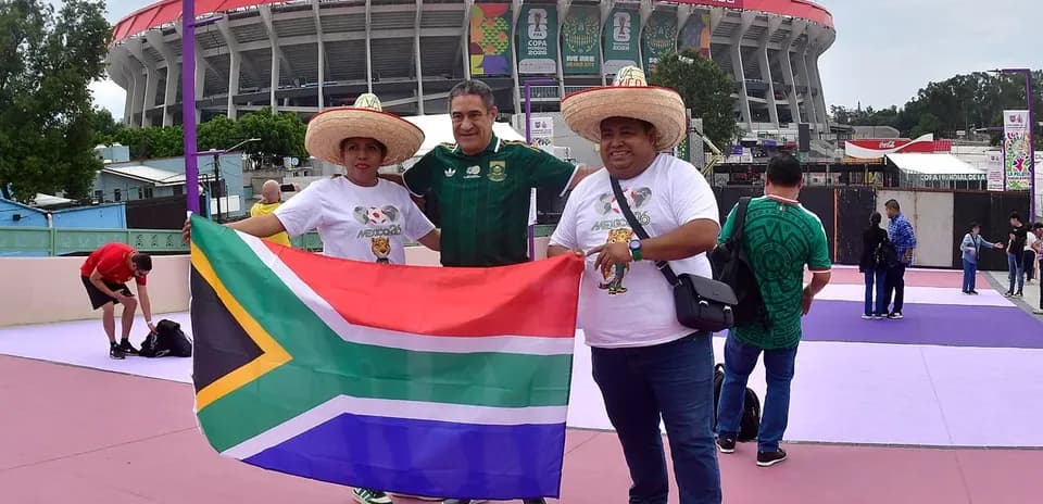 Tres aficionados sosteniendo bandera sudafricana en estadio