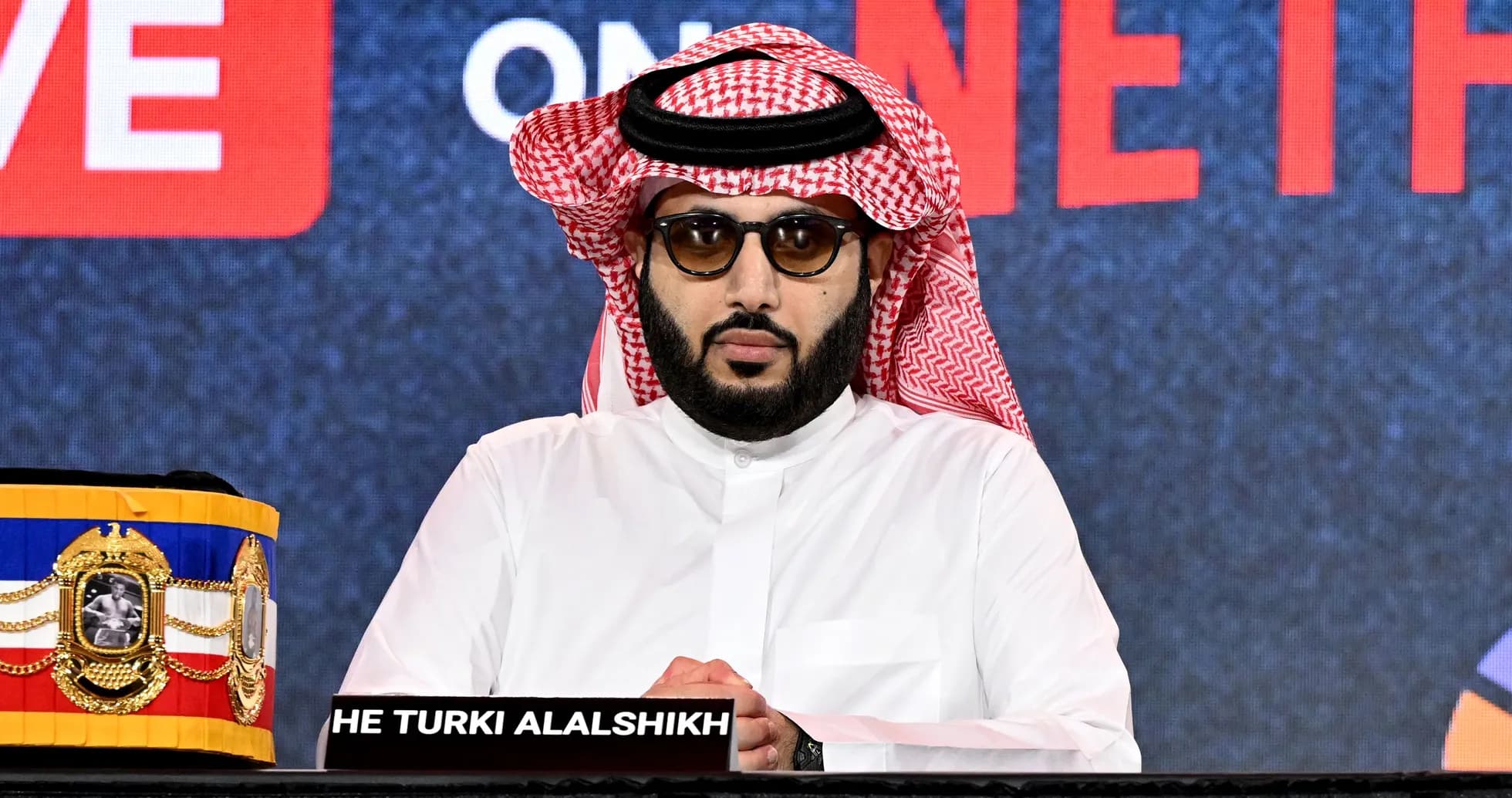 Hombre con gafas sentado en conferencia de prensa