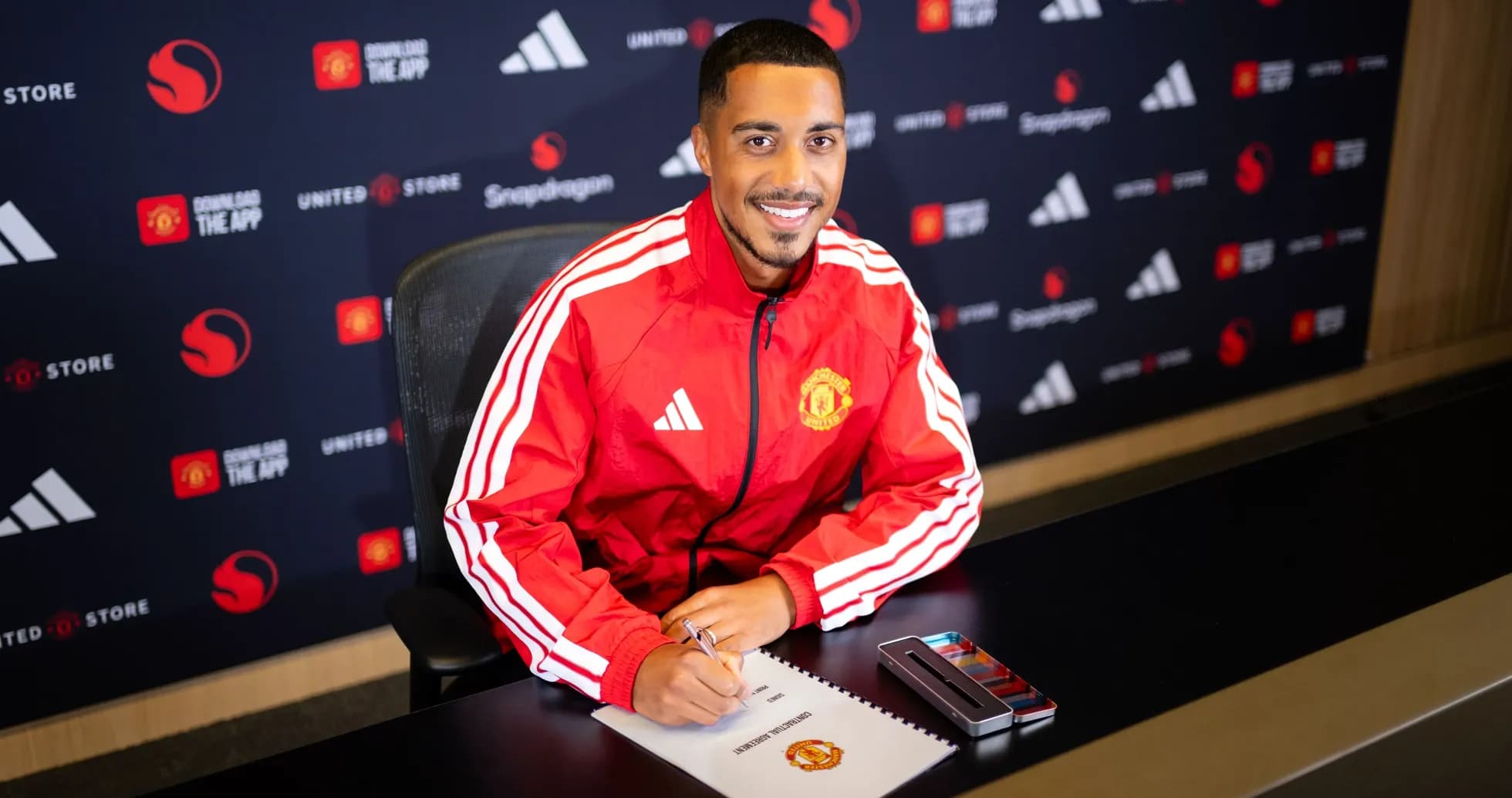 Jugador firmando contrato con Manchester United en mesa Jugador firmando contrato con Manchester United en mesa